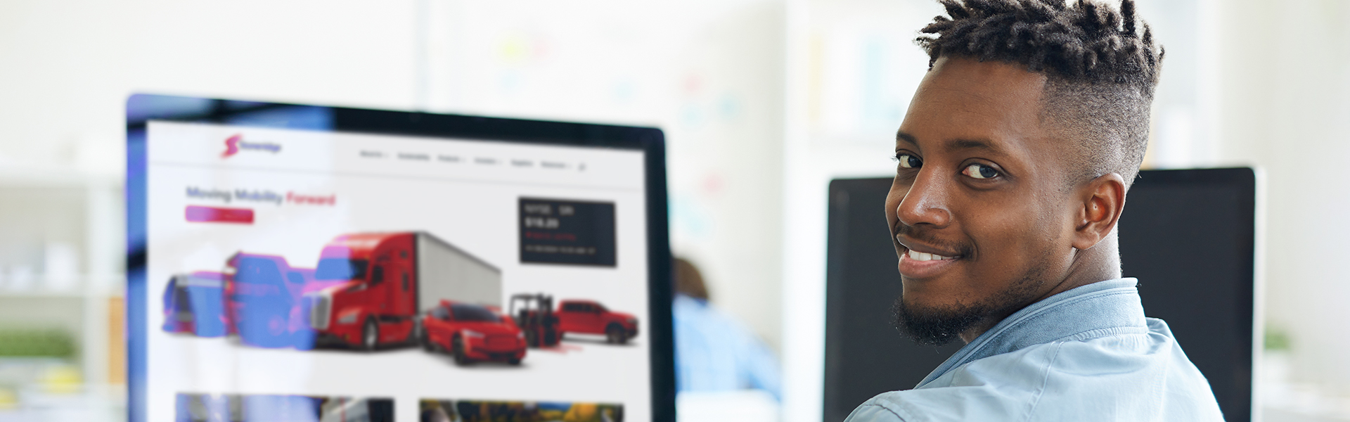 Man sitting in front of computer screen showing the Stoneridge website looking back smiling 